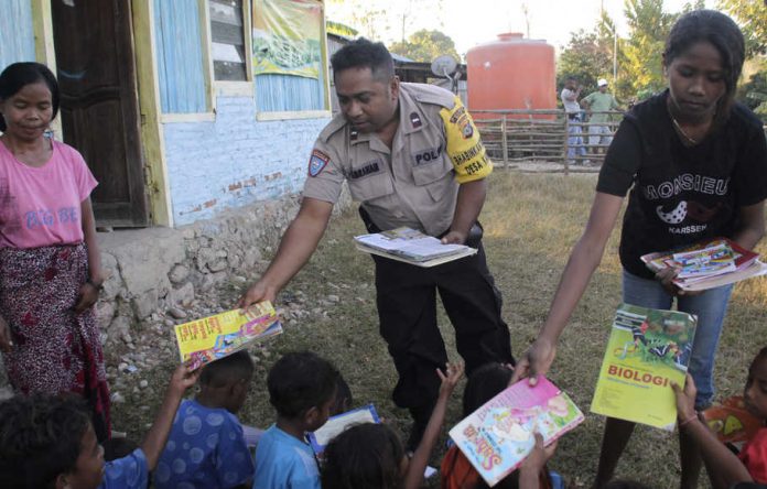 Personel Babinkamtibmas Polsek Kakuluk Mesak Aipda Abraham Doeka (tengah) didampingi seorang guru membagikan buku pelajaran dan buku bacaan kepada sejumlah anak di Desa Kabulak, Kecamatan Kakuluk Mesak, Kabupaten Belu, NTT, Selasa (9/7/2019).